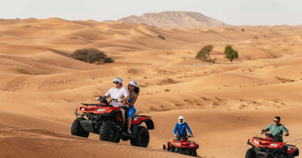 Red Dunes Desert Safari Dubai with Quad Biking – Adventurers riding quad bikes across vibrant red sand dunes at sunset